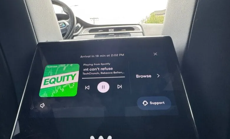 A car's infotainment screen displays the TechCrunch Equity podcast playing on Spotify, along with arrival time and controls.