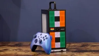 A vibrant blue Xbox controller rests beside a sleek, black AMD gaming PC with a colorful, geometric design.