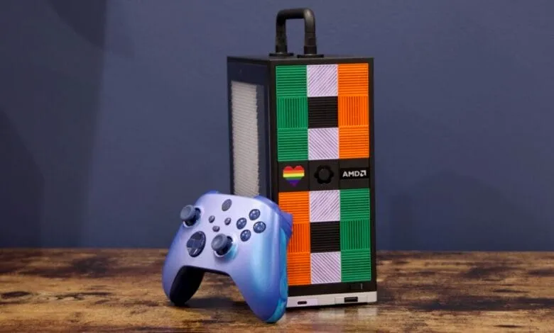 A vibrant blue Xbox controller rests beside a sleek, black AMD gaming PC with a colorful, geometric design.