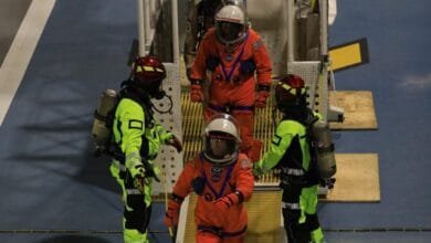 Astronauts in orange suits are assisted by safety personnel in bright green gear during a training exercise.