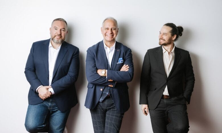 Three men in business attire stand against a white wall, exuding confidence and professionalism.