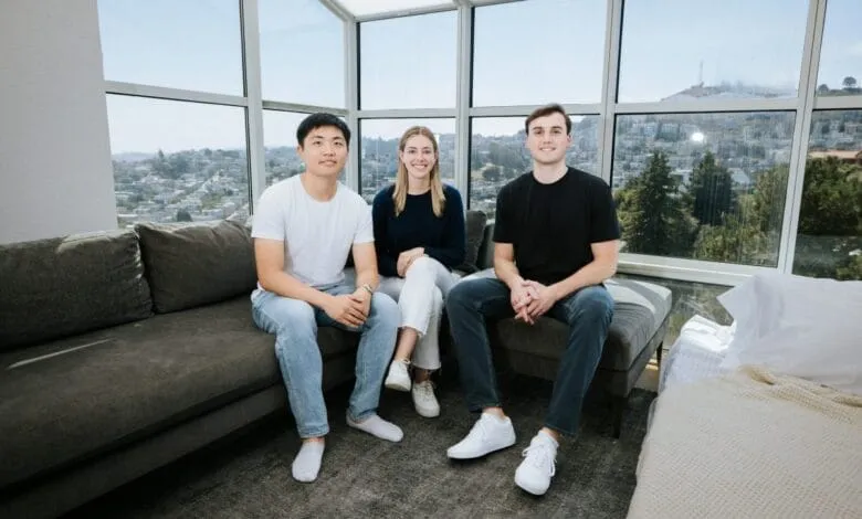 Three smiling young professionals sit on a couch, enjoying a San Francisco city view.