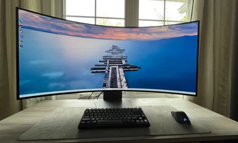 Curved ultrawide monitor displaying a serene lake and pier at sunset, with keyboard and mouse on a desk.