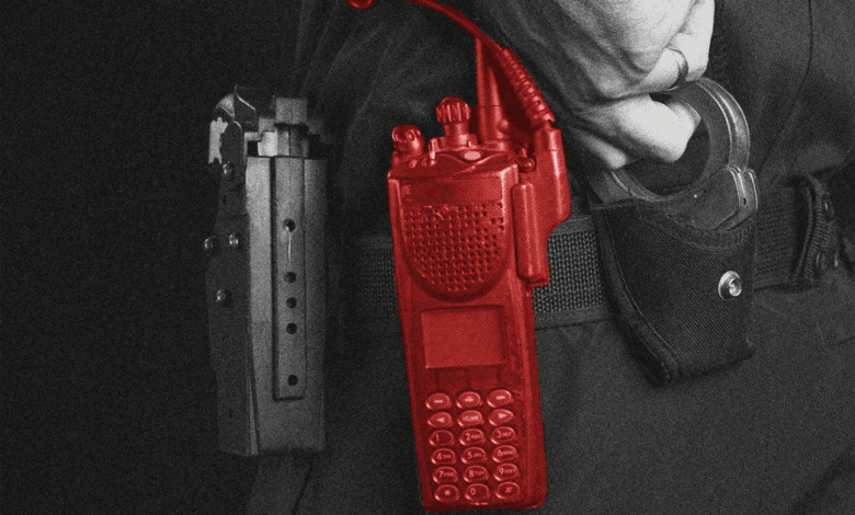 Close-up of a police officer's utility belt, showing a red radio, handcuffs, and a gun holster.