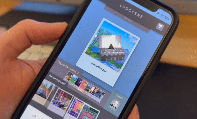 Close-up of a hand holding a smartphone displaying the Ludocene app, showcasing a Viewfinder game thumbnail.