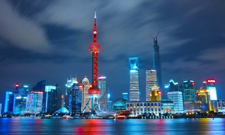 Vibrant nighttime cityscape of Shanghai, China, featuring the iconic Oriental Pearl Tower and modern skyscrapers illuminated in blue and red.