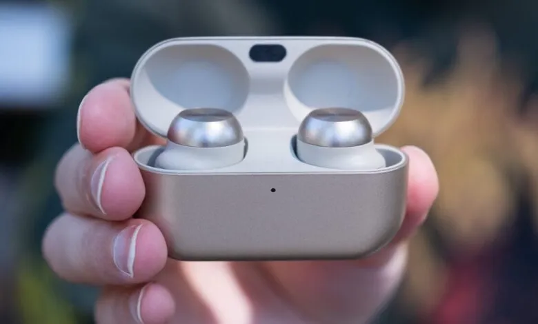 A hand holds open a Technics EAH-AZ100 earbuds case, revealing two silver earbuds.