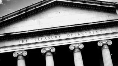 Black and white close-up of the US Treasury Department building's facade, featuring ionic columns and engraved lettering.