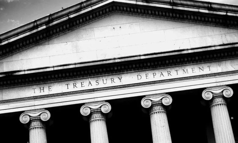 Black and white close-up of the US Treasury Department building's facade, featuring ionic columns and engraved lettering.