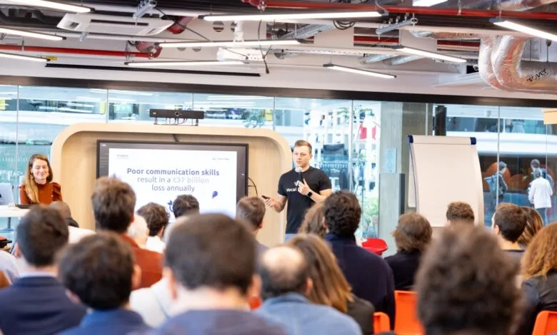 Speaker presenting at AI startup launch event, large audience listening attentively.