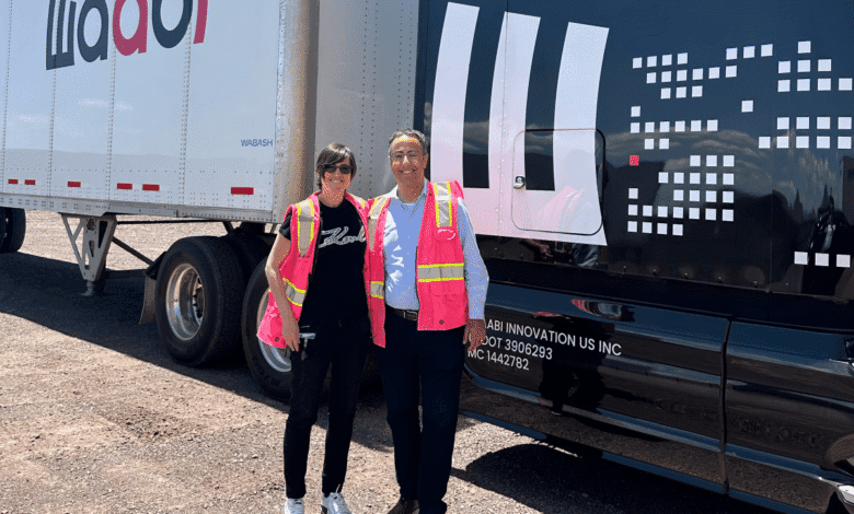 Two people in pink safety vests stand proudly in front of a Waabi self-driving truck.