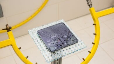 Smartphone undergoing water resistance test, covered in water droplets.