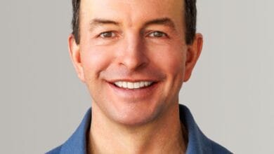 Headshot of a smiling man in a blue polo shirt against a gray background.
