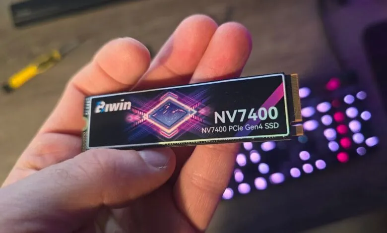 Close-up of a hand holding a Biwin NV7400 PCIe Gen4 SSD, a small black computer component with purple and pink accents.