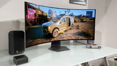 Cyberpunk 2077 gameplay shown on a curved monitor, alongside speakers and a model car.