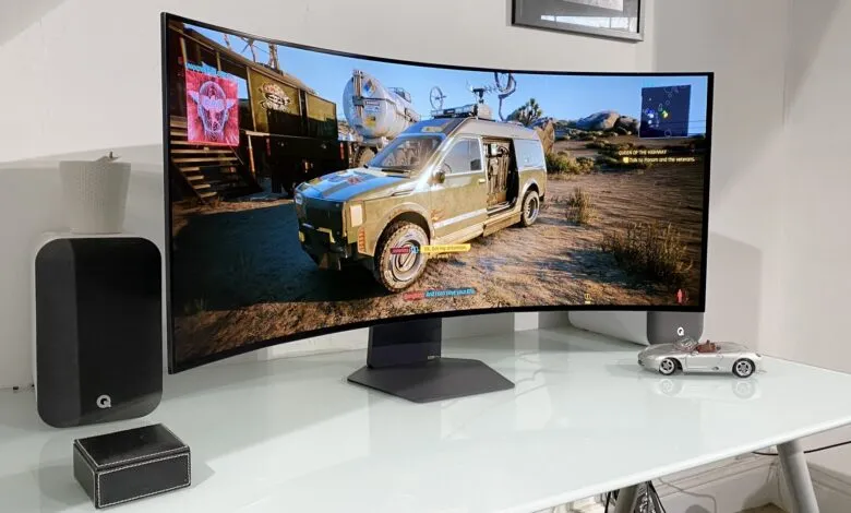 Cyberpunk 2077 gameplay shown on a curved monitor, alongside speakers and a model car.