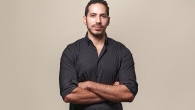 Portrait of a man with arms crossed, wearing a black shirt against a beige background.