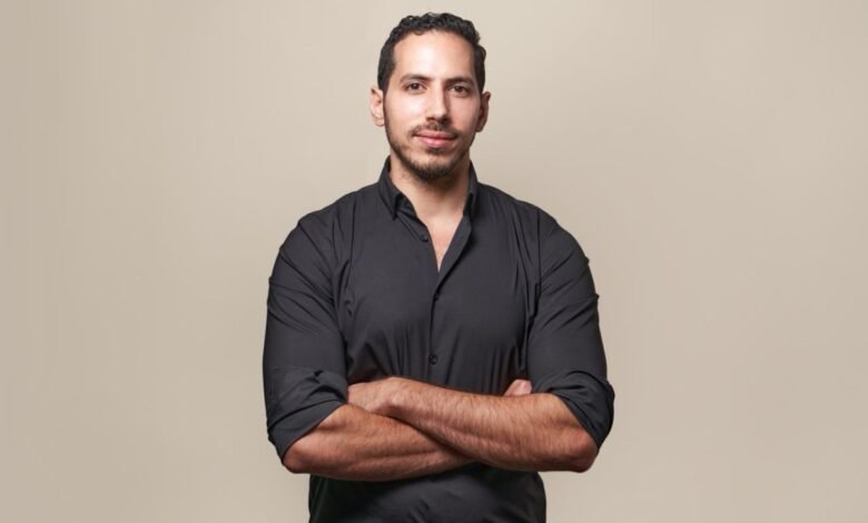 Portrait of Khalid ,Ashmawi, with arms crossed, wearing a black shirt against a beige background.