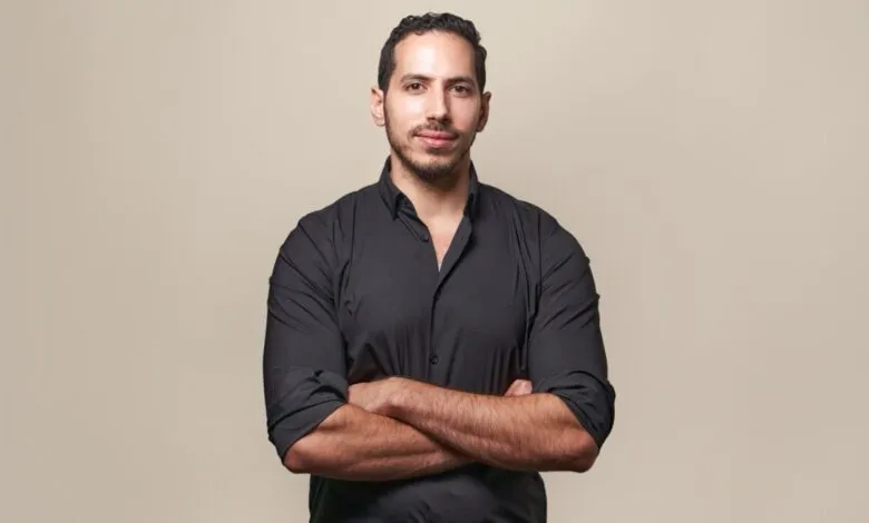 Portrait of Khalid ,Ashmawi, with arms crossed, wearing a black shirt against a beige background.