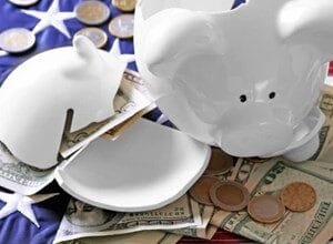 Broken piggy bank with US currency and coins on an American flag, symbolizing financial hardship.