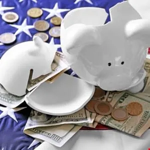 Broken piggy bank with US currency and coins on an American flag, symbolizing financial hardship.