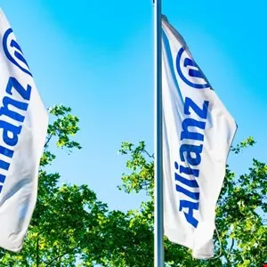 Two Allianz flags waving against a bright blue sky and lush green trees.