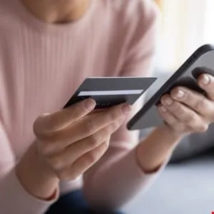 Close-up of hands holding a credit card and smartphone, making an online payment.