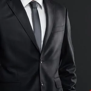 Close-up of a man in a dark suit and tie against a black background.