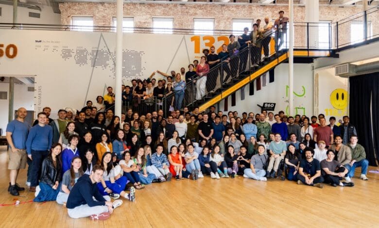 Large diverse group of employees posing for a photo in a modern office with exposed brick walls and a large wall graphic.