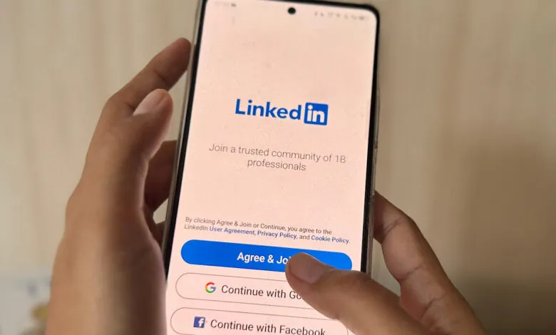 Close-up of a hand holding a smartphone displaying the LinkedIn login screen, finger about to tap 'Agree & Join'.