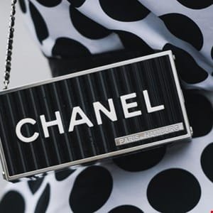 Close-up of a black Chanel clutch with a silver frame, featuring the brand name in white lettering.