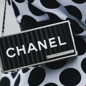Close-up of a black Chanel clutch with a silver frame, featuring the brand name in white lettering.