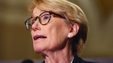 Close-up of Senator Maggie Hassan speaking, wearing glasses and a dark jacket.