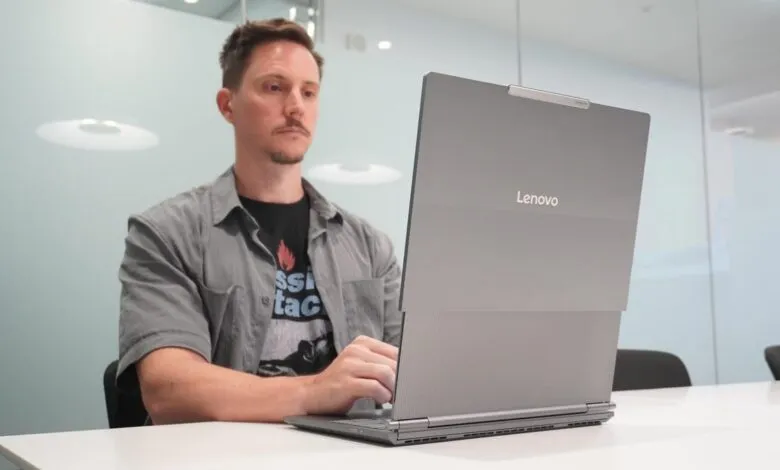 Person using a silver Lenovo laptop in a modern office.