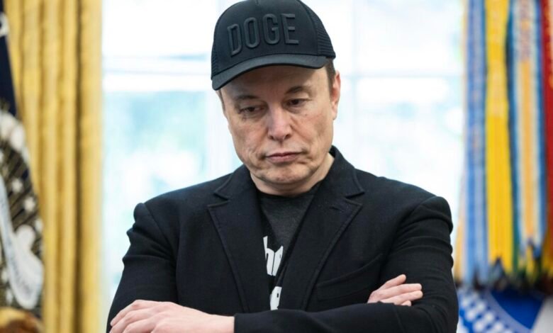 Elon Musk, wearing a black 'DOGE' hat, stands with arms crossed in the Oval Office.