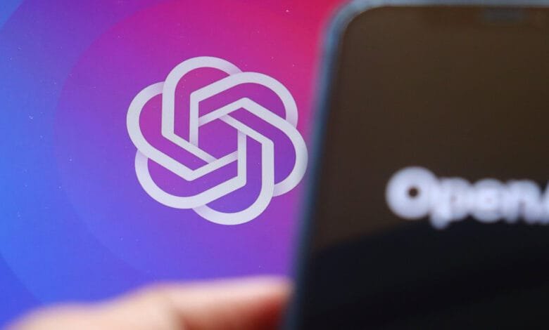 Close-up of OpenAI logo on a screen, partially obscured by a smartphone displaying the OpenAI text.