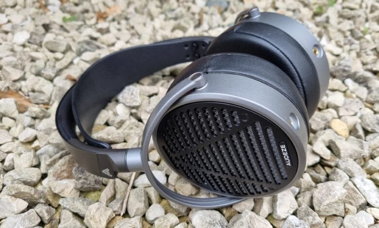 Audeze headphones rest on a bed of gray gravel. The headphones are gray and black with a unique patterned earcup.