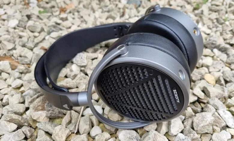 Audeze headphones rest on a bed of gray gravel. The headphones are gray and black with a unique patterned earcup.