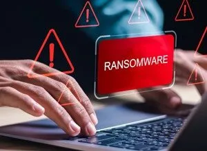 Close-up of hands on laptop with a ransomware warning, red alert triangles surround the screen.