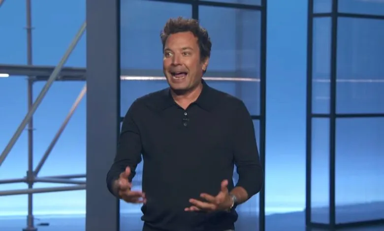 Jimmy Fallon, energetic and expressive, speaks on a TV set with a blue backdrop.
