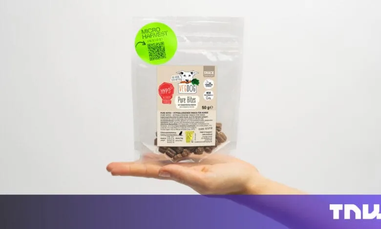 A hand holds a small bag of VegDog Pure Bites, a hypoallergenic dog snack. The bag features a QR code and product details.