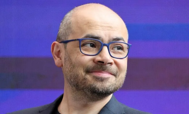 Headshot of a balding man with glasses, slightly smiling, against a purple background.