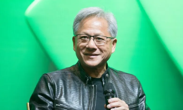 Jensen Huang, Nvidia CEO, smiles while holding a microphone against a green background.