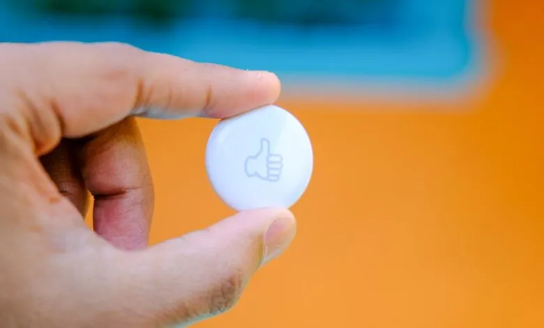 Close-up of a hand holding a small, white button with a thumbs-up icon.