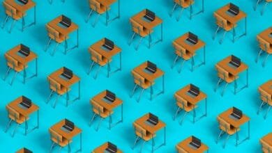 Repeating pattern of student desks with laptops on a bright blue background. Illustrates online learning or a classroom setting.