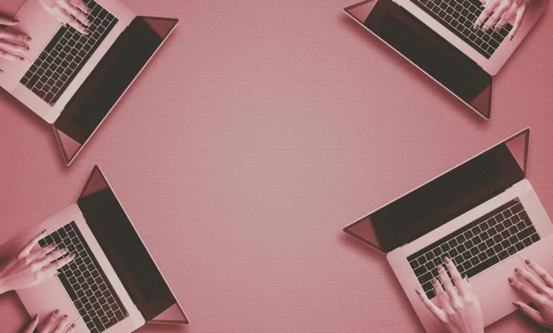 Four laptops arranged on a pink surface, with hands typing on each. Space for text in the center.