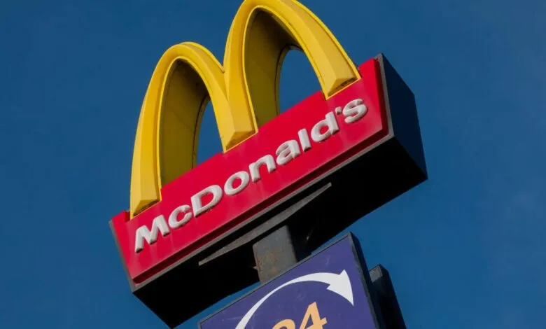 Iconic McDonald's golden arches logo on a red sign against a clear blue sky.