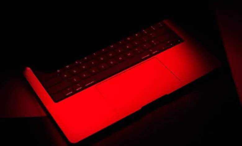 Red-lit laptop keyboard in low light; keys and trackpad glow intensely.