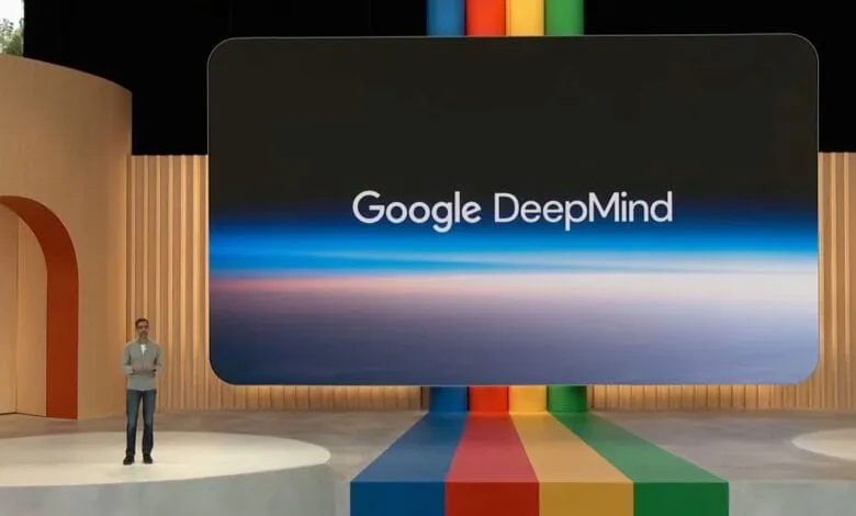 A speaker presents on stage at Google I/O 2023, a large screen behind him displays the Google DeepMind logo against a sky backdrop.