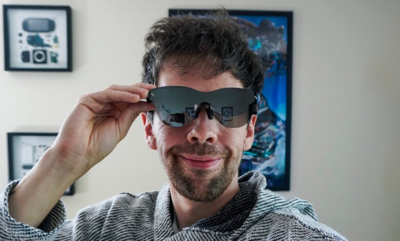 Man wearing futuristic sunglasses and adjusting them, smiling at the camera.